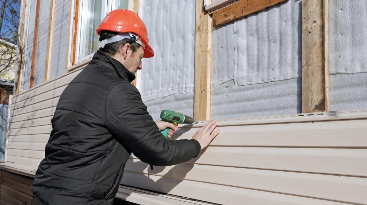 Siding replacement professional using a power drill to install new tan vinyl siding on a home exterior in Marietta, GA
